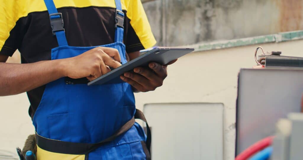 HVAC technician inspecting an outdoor air conditioning unit with a tablet