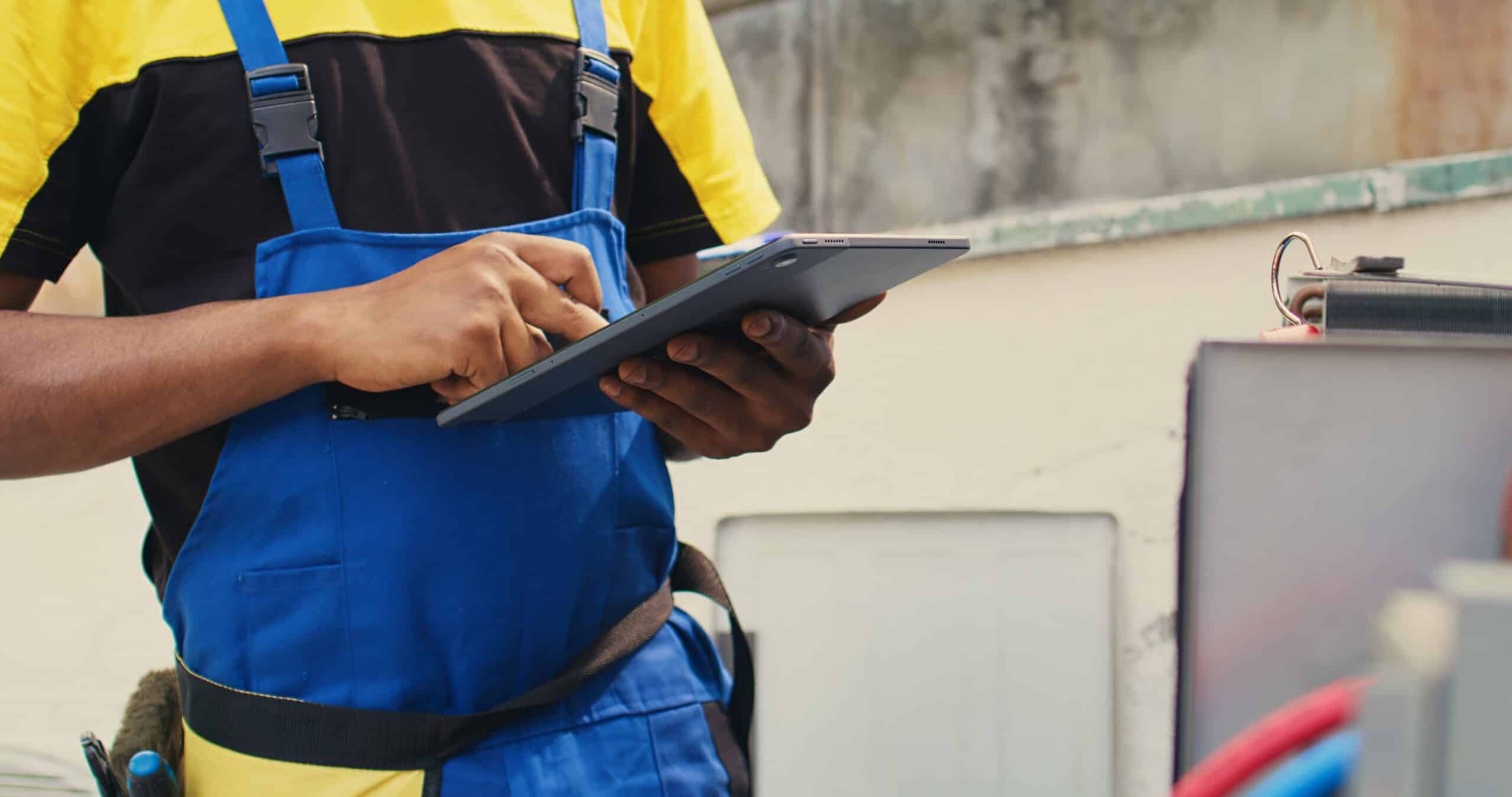 HVAC technician inspecting an outdoor air conditioning unit with a tablet