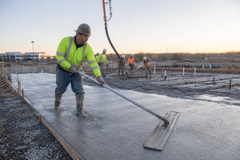 Concrete finisher leveling fresh concrete on a large outdoor slab with a construction crew
