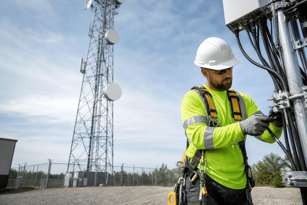 Tower technician working on wireless equipment beside a communication tower